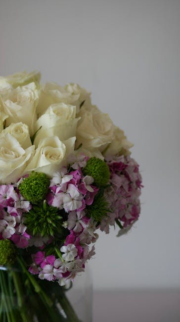 A close-up view of a floral arrangement featuring a bouquet of fresh white roses with tightly layered petals, complemented by clusters of vibrant pink and white hydrangeas, and accented with small, br