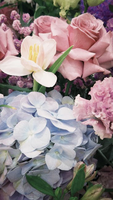 A vibrant display of floral arrangements featuring various types of flowers, predominantly roses in shades of pink, white, and cream, alongside clusters of small white blossoms and larger purple flowe